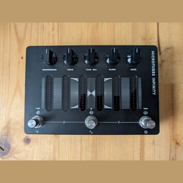 Černý kytarový efekt s nápisem MICROTUBES INFINITY. V horní části jsou pět otáčivých ovladačů s popisky COMPRESSION, DRIVE, TONE • ERA, BLEND a LEVEL…