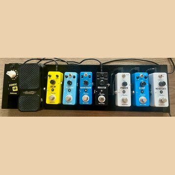 Sada efektů na černém pedalboardu. Zleva jsou vidět pedály s nápisy: SONIC IR (SONICCAKE), VOLWAH, DELAY (Rowin), AC STAGE (Rowin), HARMONIZER (Rowin…