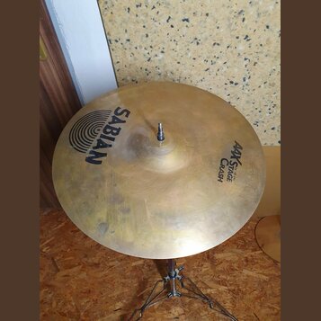 Zlatý činel typu crash umístěný na kovovém stojanu. Na povrchu jsou čitelné nápisy SABIAN a AAX STAGE CRASH 16"/40cm. Povrch vykazuje drobné nečistot…