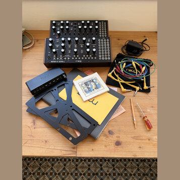 Na fotografii jsou dva černé syntezátory s nápisem Moog, z nichž na spodním je uveden model MOTHER-32 SEMI MODULAR ANALOG SYNTHESIZER. Součástí sady…
