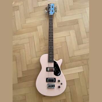 Světle růžová elektrická basová kytara s tmavým hnedým hmatníkem. Na hlavě nástroje je nápis GRETSCH a na černé plechovce u snímačů je rovněž logo GR…