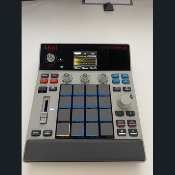 Šedý sampler MPC SAMPLE značky AKAI professional. Zařízení má v horní části displej s vizualizací zvukové vlny, ovládací knoflíky a v pravé části 16…