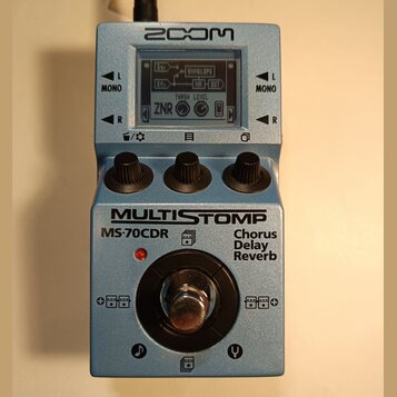Modrý efektový pedál značky ZOOM s nápisem MULTISTOMP MS-70CDR Chorus Delay Reverb. Na horní straně je LCD displej zobrazující řetězec efektů včetně…