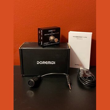 Černý MIDI pedál s nápisy DOREMIDI a MIDI Foot Controller FC-ONE. Vedle něj je černá krabice s bílým nápisem DOREMIDI a bílý manuál s textem MIDI脚踏控制…