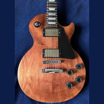 Elektrická kytara s hnědým dřevěným povrchem a černým plechtrátem. Nástroj má dva humbuckery s kovovými kryty, čtyři černé otočné knoflíky a přepínač…