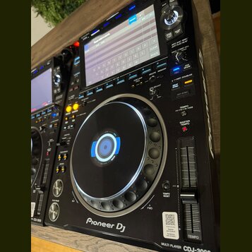 Černý digitální DJ player s displejem a velkým ovládacím jog-kolem. Na přístroji jsou viditelné nápisy Pioneer DJ a MULTI PLAYER CDJ-3000. Povrch je…