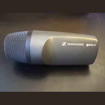 Šedý dynamický mikrofon s kovovou síťkou. Na těle je bílý nápis SENNHEISER s logem a označení e602-II. Povrch mikrofonu je matný a v dobrém stavu.
