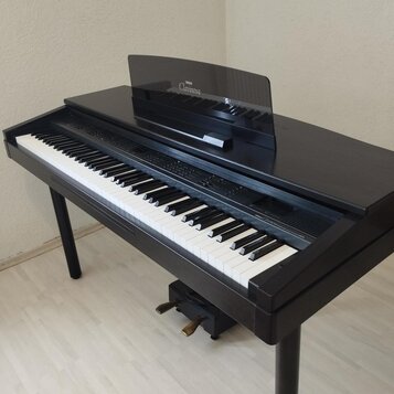 Černé digitální piano s klaviatura v klasickém provedení. Na hudebním stojanu je bílý nápis Clavinova a nad ním menší logo Yamaha. Nástroj je umístěn…
