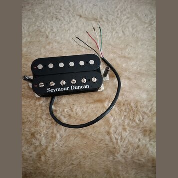 Černý humbucker s kovovou základnou a čtyřmi barevnými vodiči. Na spodním plastovém krytu je bílý nápis Seymour Duncan. Snímač vykazuje mírné známky…
