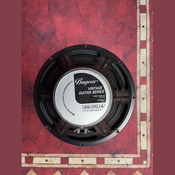 Kruhový reproduktor s černým rámem a bílým štítkem v centru. Na štítku je uveden nápis Bugera™, VINTAGE GUITAR SERIES, POWER HANDLING 100 Watt, IMPED…