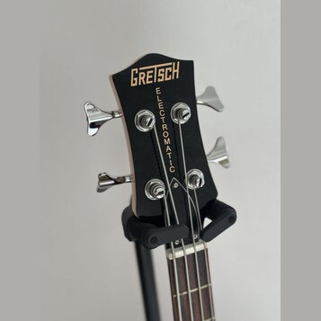 Černá hlava basové kytary s nápisem GRETSCH v horní části a svislým nápisem ELECTROMATIC pod ním. Nástroj má čtyři chromované ladičky. Povrch je hlad…