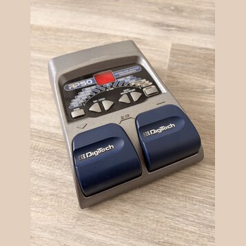 Šedý kytarový procesor s nápisem RP50 a MODELING GUITAR PROCESSOR. Zařízení má červený displej, řadu ovládacích tlačítek a dvě modrává pedály s bílým…