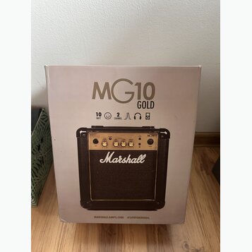 Krabice s kytarovým kompem, na které je velký nápis MG10 GOLD. Pod ním jsou ikony a texty 10 WATT, 6.5", 2 CHANNEL spolu s ikonami sluchátek a reprod…