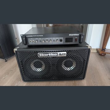Černý basový zesilovač Hartke LH1000 1000 WATT BASS AMPLIFIER CLASS A VALVE PREAMP položený na černém basovém reproduktoru Hartke HL210 HyDrive. Zesi…