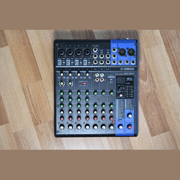Černý mixovací pult s modrými prvky a bílými nápisy. Na přístroji je viditelné logo YAMAHA a označení modelu MG10XU MIXING CONSOLE. V pravé části se…