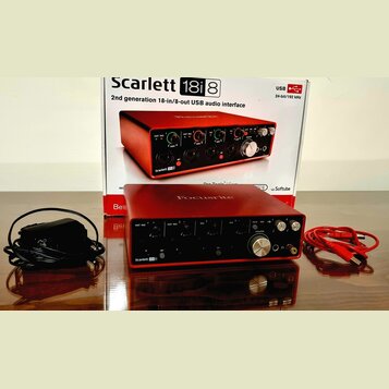 Červená USB audio rozhraní Focusrite Scarlett 18i8 s kovovým povrchem. Na přední straně jsou vidět regulační knofíky, přepínače a konektory. Vedle za…