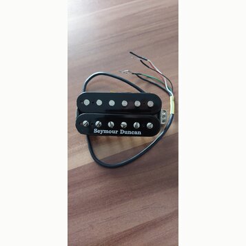 Černý humbucker s kovovými póly a bílým nápisem Seymour Duncan. Nástroj má připojený kabel s několika barevnými vodiči. Povrch je lesklý a vykazuje m…