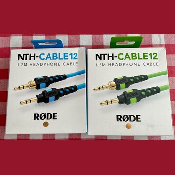 Dvě krabičky s nápisy NTH-CABLE12 a 1.2M HEADPHONE CABLE. Na obalech je logo RØDE a fotografie kabelů v modré a zelené barvě. Krabičky jsou bílé s ba…