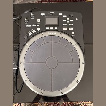Černý elektronický perkusní pad značky Roland. Na zařízení je nápis HANDSONIC Expr/NATURAL a označení modelu HPD-20. Horní část obsahuje displej, ovl…