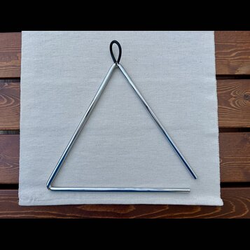 Kovový trojúhelník stříbrné barvy s černou šňůrkou v horním vrcholu. Nástroj je položen na světlé látkové podložce, která leží na dřevěném stole. Na…
