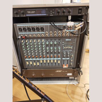 V hliníkovém racku jsou umístěna tři zařízení. V horní části je digitální reverb s nápisem REV100 DIGITAL REVERBERATOR, ve středu míchací pult YAMAHA…