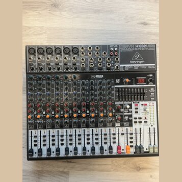 Černý mixovací pult značky behringer, model XENYX X1832USB. Zařízení obsahuje více vstupních kanálů s potenciometry, posuvníky a digitální displej v…