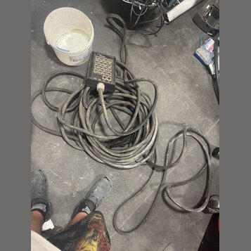 Na fotografii je zmotaný šedý kabel s připojeným černým ovládacím boxem. Box obsahuje 12 tlačítek a nápisy „SMLART“, „TX“ a „RX“. Povrch kabelu i box…
