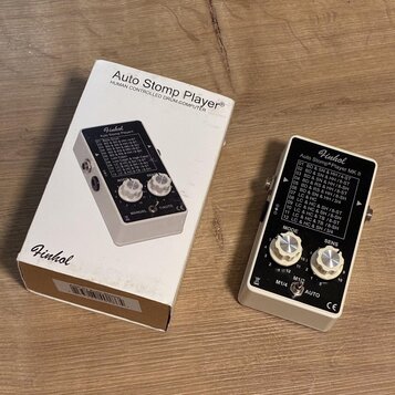 Bílá krabice s nápisem Auto Stomp Player® HUMAN CONTROLLED DRUM COMPUTER a logem Finhol. Vedle krabice je bílý efekt pedál značky Finhol s označením…