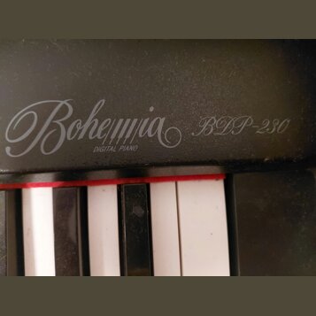 Detailní záběr na černý digitální klavír. Na povrchu je bílým nápisem uveden název Bohemia, pod kterým je menším písmem DIGITAL PIANO a vedle modelu…