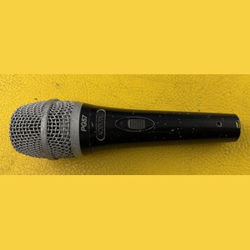 Černý dynamický mikrofon s kovovou stříbrnou mřížkou. Na těle je bílý nápis PG57 a logo SHURE v oválném rámečku. Povrch těla vykazuje drobné nečistot…