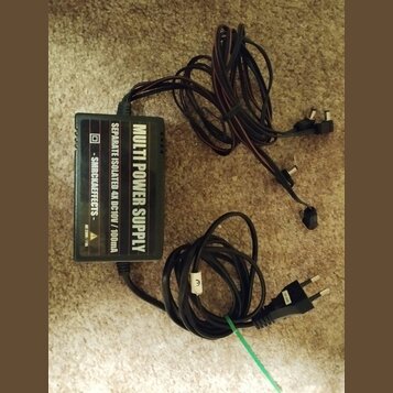 Černý napájecí adaptér s nápisem MULTI POWER SUPPLY a SEPARATE ISOLATED 4X DC10V / 100mA. Na boku je uveden text - SMRCKAEFFECTS - a označení DC 230V…