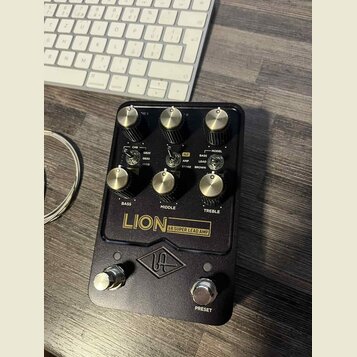 Černý kytarový předzesilovač s kovovým šasi a zlatými ovládacími knoflíky. Na předním panelu jsou nápisy LION 68 SUPER LEAD AMP, BASS, MIDDLE, TREBLE…