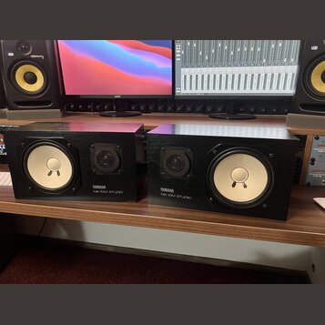 Dva studiové monitory v černých hranatých bednách. Na přední straně každého reproduktoru je bílý nápis YAMAHA a pod ním NS-10M STUDIO. Oba mají jeden…