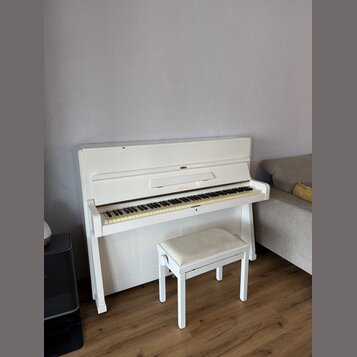 Bílé piano s doprovodnou bílou stoličkou s béžovým polstřením. Na přihradce nad klávesami je vidět nápis PETROF. Nástroj vykazuje mírné opotřebení v…