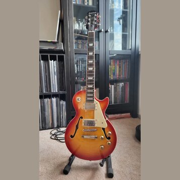 Polodupatá elektrická kytara s trupem v červeno-žlutém sunburst provedení a bílým pickguardem. Na hlavě hmatníku je bílý nápis Epiphone a červené log…