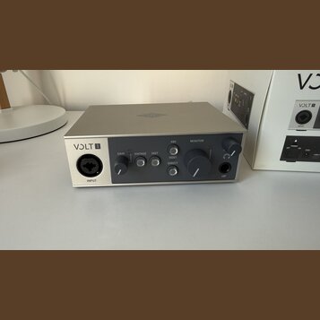 Stříbrnošedý audio rozhraní s nápisem VOLT 1 na levé straně. Přední panel obsahuje vstup INPUT, knoflík GAIN, tlačítka VINTAGE a INST, přepínač HOST…