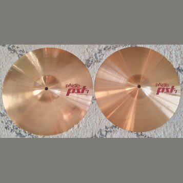 Dvě mosazné činely typu hi-hat položené vedle sebe na šedém koberci. Levý činel nese nápisy pAiste, pst 7 a 14" HEAVY HI-HAT TOP. Pravý činel má nápi…