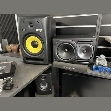 Na fotografii jsou tři studiové monitory a jeden mixér. Největší černý reproduktor má žlutý membránový basový reproduktor a nápisy KRK a ROKIT 8. Ved…