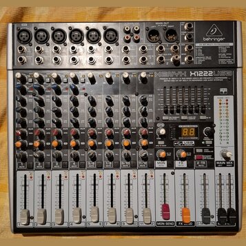 Stříbro-šedý mixážní pult značky behringer s nápisem XENYX X1222USB. Zařízení obsahuje 6 mikrofonních vstupů, několik linkových vstupů a faderové ovl…