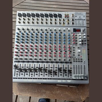 Stříbrný mixážní pult s nápisem EUROBACK UR244FX-PRO. Zařízení obsahuje několik vstupních kanálů s modrými a červenými otočnými knoflíky, posuvníky h…
