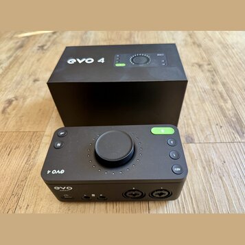 Černý audio rozhraní s velkým centrálním ovladačem a několika tlačítky. Na zařízení jsou nápisy „evo 4“, „EVO AUDIENT“ a označení tlačítek „48V“, „1“…