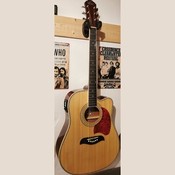 Akustická kytara s přístupem pro praváky, přírodní barva těla a tmavě hnědá hlava. Na hlavě je viditelné logo Epiphone. Kytara má červený pickguard a…