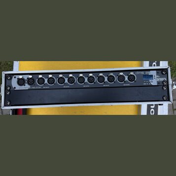 Černý rackový přístroj s nápisy dmx merger/splitter a dms 26. Na předním panelu se nachází šest skupin konektorů, z nichž každá obsahuje jeden vstup…
