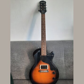 Elektrická kytara s tělem v žlutém sunburst provedení a černým pickguardem. Na hlavě hředu je bílý nápis Epiphone a pod ním nápisy Junior a Les Paul.…