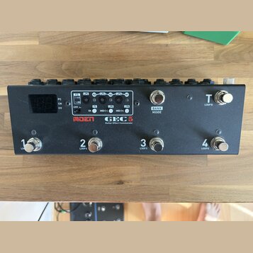 Černý kytarový spínací pedalboard s nápisy MOEN a GEC 5 Guitar Effect Commander. Zařízení má čtyři spodní spínače označené čísly 1, 2, 3 a 4 s doplňk…