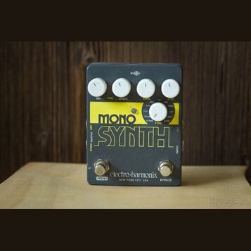 Šedý efekt pedál s žlutým nápisem MONO SYNTH. Na horní části jsou čtyři bílé oválné knoflíky s popisky DRY VOL, SYNTH, SENS a CTRL. Uprostřed je jede…