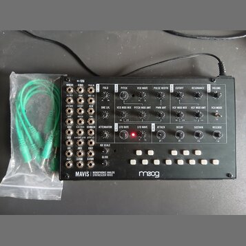 Černý analogový syntetizátor s bílými nápisy a ovládacími prvky. Na spodní liště je uveden název MAVIS MONOPHONIC ANALOG SYNTHESIZER VOICE a logo moo…