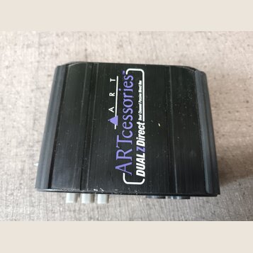 Černý obdélníkový box z plastu s texturovaným povrchem. Na horní straně je bílý a fialový nápis ARTcessories TM DUAL Z Direct Dual Channel Passive Di…
