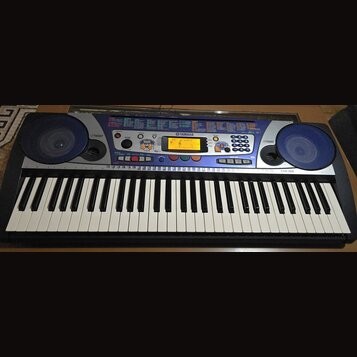 Elektronický klavír v černé barvě s modrým ovládacím panelem a dvěma integrovanými reproduktory po stranách. Na panelu je viditelné logo YAMAHA a ozn…