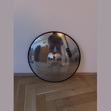 Kruhové kovové perkusní pomůcky s perforovaným povrchem a černým okrajem. Uprostřed se nachází vyvýšený kopulek. Povrch je zasrcálený a reflexní, bez…